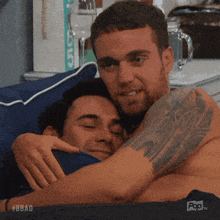 two shirtless men hugging each other on a bed with a bbc logo in the background