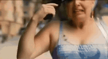 a woman in a blue tank top is talking on a cell phone while wearing sunglasses .