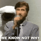 a man singing into a microphone with the words we know not why below him .