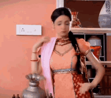 a woman in a pink and red dress is standing in front of a shelf with vases on it .