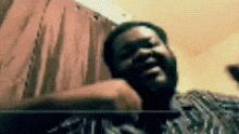 a man with a beard is sitting in front of a curtain and looking at the camera .