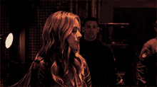 a woman in a leather jacket stands in front of a man