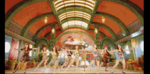 a group of women are dancing in a large room with a green ceiling