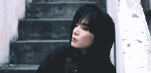a young man wearing a black hoodie is leaning against a wall and stairs .