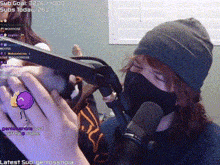 a person wearing a mask is holding a gun in front of a microphone while another person looks on .