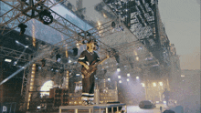 a man playing a bass guitar on a stage with a large screen behind him