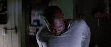 a man in a gray shirt is standing in a dark room and looking down .