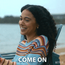 a woman in a striped sweater is sitting in a chair and smiling with the words come on behind her