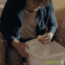 a man is sitting on a chair eating a piece of food from a trash can that says shameless