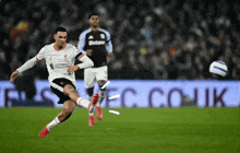 a soccer player is kicking a ball in front of a sign that says betano