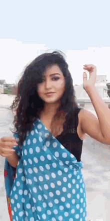 a woman wearing a blue polka dot saree and a black bra is standing on a rooftop .
