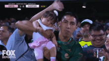 a man holds a baby in front of a scoreboard that says queretaro on it