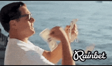 a man is holding a bunch of money in front of the ocean with rainbet written in the corner
