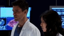 a man and a woman are standing in front of computer monitors looking at something .