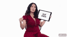 a woman in a red dress is sitting in a chair holding a tablet with the words `` que onda '' on it .