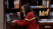 a woman sits at a desk using a laptop with netflix written on the bottom