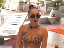 a woman in a leopard print bikini and black sunglasses is sitting at a table