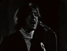 a black and white photo of a man singing into a microphone in a dark room