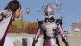 a woman stands next to a purple and black superhero with a helmet on