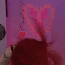 a woman with red hair is standing in front of a pink wall with a heart sticker on it .
