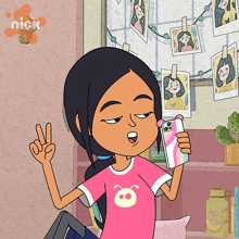 a girl in a pink shirt is holding a cell phone in front of a wall with pictures of girls hanging on it