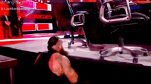 a wrestler is laying on the floor next to a chair .