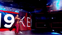 a wrestler is walking on a stage with the number 19 on the wall behind him