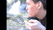 a young man is smoking a cigarette outside in the woods