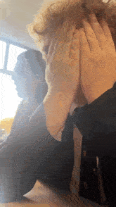 a man in a suit is covering his face with his hands while sitting at a table .