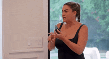 a woman in a black tank top is holding a cell phone in her hands .