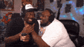 two men wearing headphones are laughing and one has a hat that says let 's smoke it
