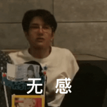 a man wearing glasses and a white shirt is sitting on a couch with chinese writing on his face .