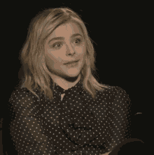 a woman wearing a black and white polka dot shirt is sitting in a chair .