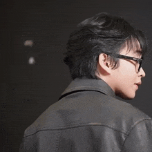 a young man wearing glasses and a leather jacket looks at the camera