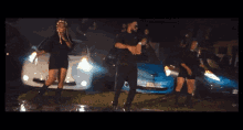 a man and a woman are dancing in front of a blue car with a license plate that says aa - nz