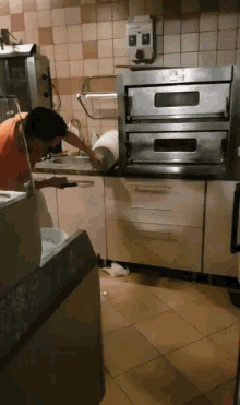 a man in an orange shirt is working in a kitchen in front of a double oven