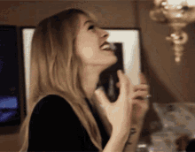 a woman in a black dress is laughing and holding a glass of wine