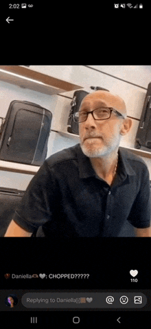 a man with glasses and a beard is sitting in front of a shelf of luggage