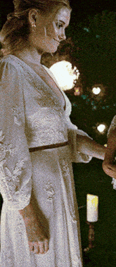 a woman in a white dress is standing in front of a candle holder