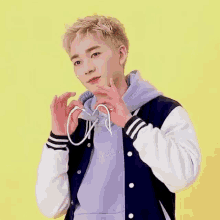 a young man is making a heart shape with his hands while wearing a baseball jacket .