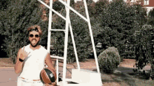 a man wearing sunglasses and a headband is holding a basketball in front of a basketball hoop .