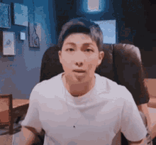 a man in a white t-shirt is sitting in a chair and making a funny face .