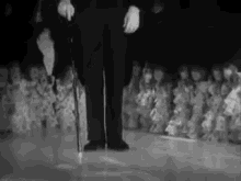a man in a tuxedo is holding a cane in front of a crowd of people .