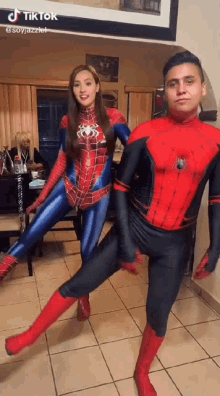 a man and a woman in spiderman costumes are dancing together in a living room .