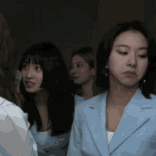 a group of women are standing in a dark room and one woman is wearing a blue jacket