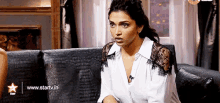 a woman in a white shirt is sitting on a couch with a microphone .