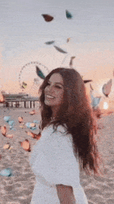 a woman in a white dress is standing on a beach with butterflies falling around her .