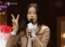 a girl in a school uniform is holding a microphone and giving the peace sign