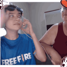 a boy wearing a blue free fire shirt talks on a phone