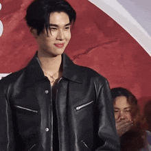 a young man wearing a black leather jacket is standing in front of a red wall